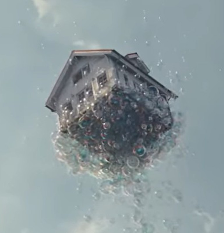 Ein Haus wird von vielen Seifenblasen in den Himmel gehoben.